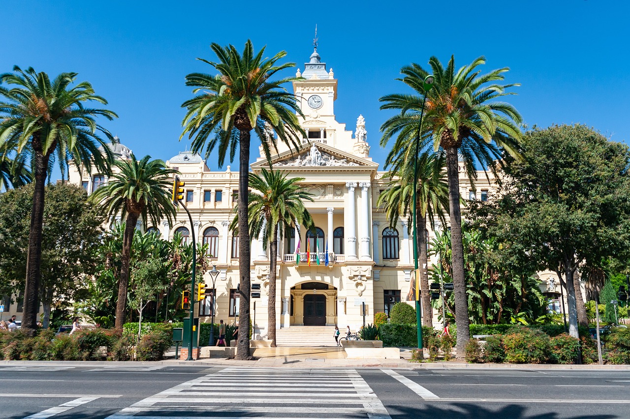A white building with palm trees and a clock tower along a street.
