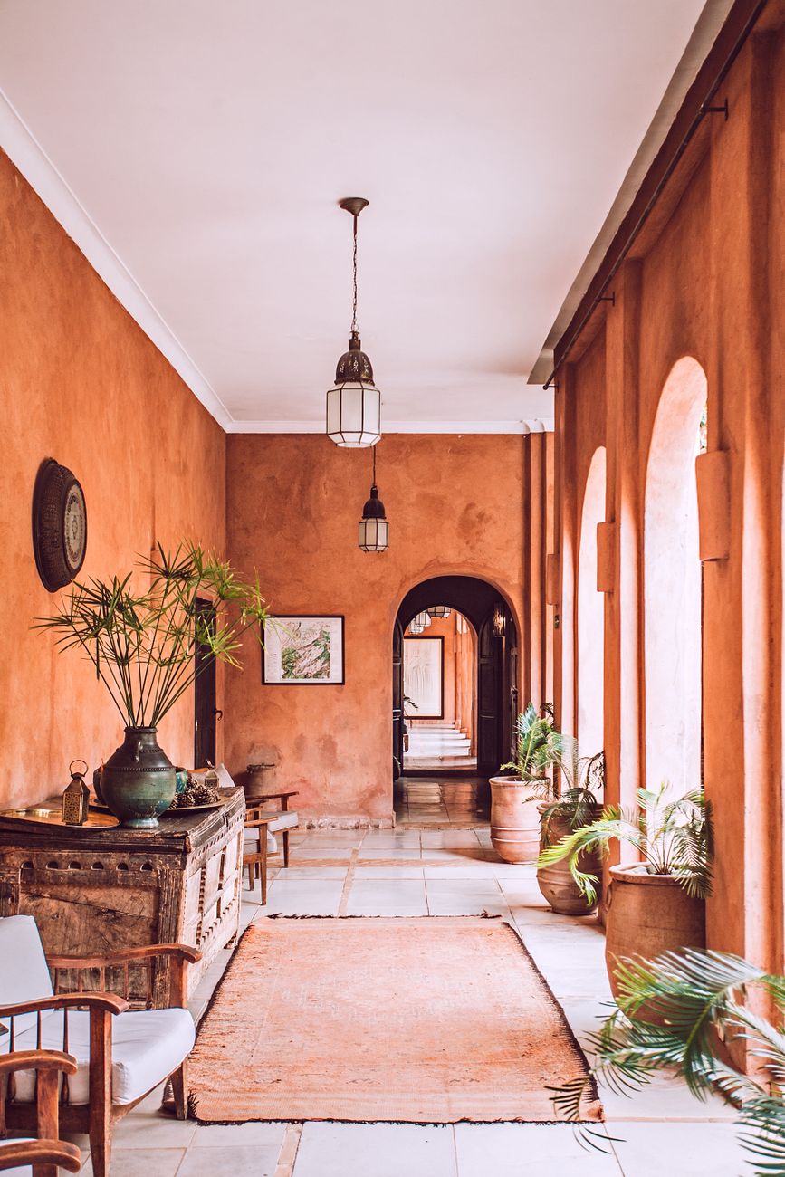 A terracotta-walled hallway with arches and rustic wooden furniture.